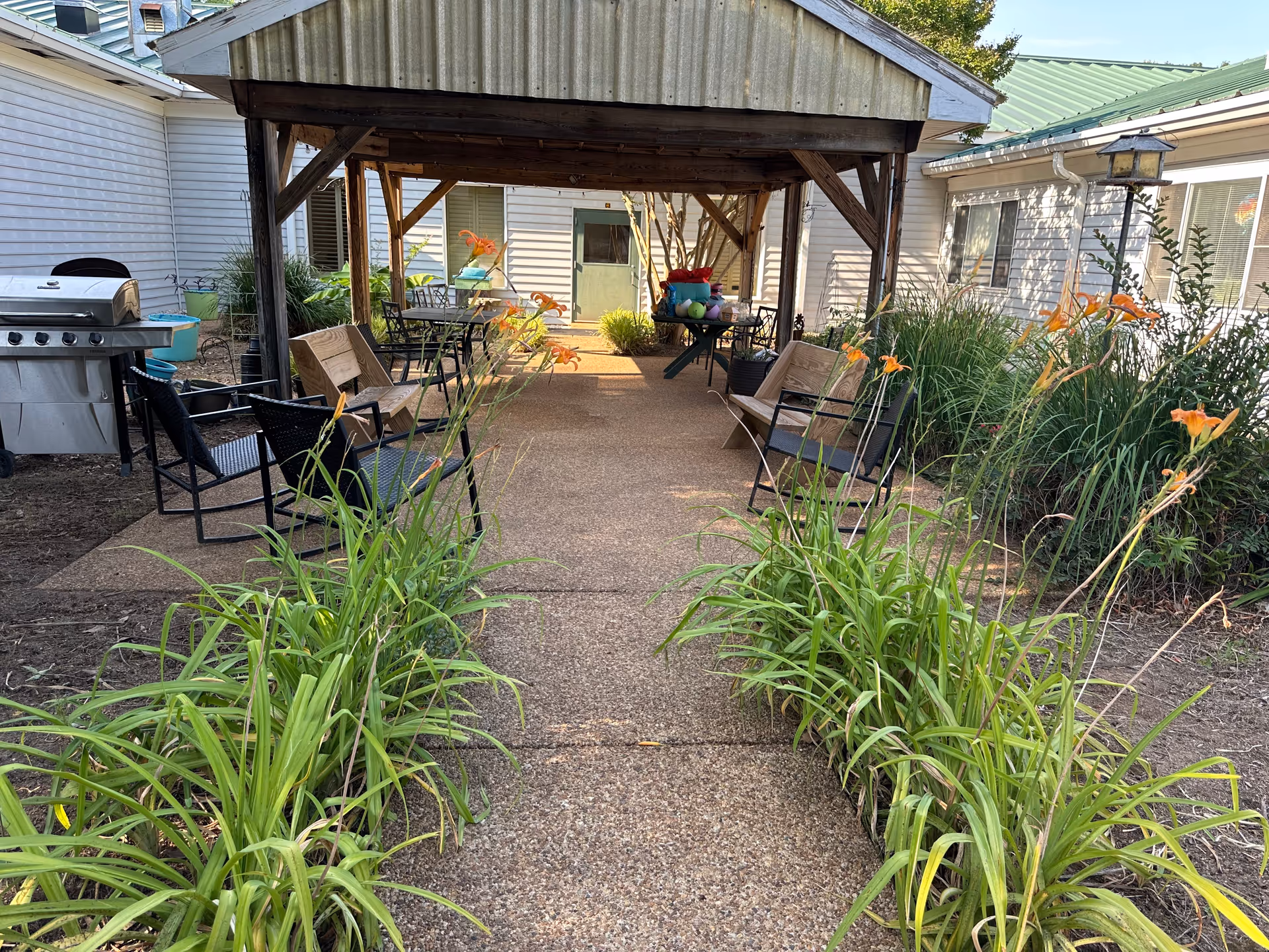 Outdoor courtyard with a covered seating area, benches, and tall plants along a path.