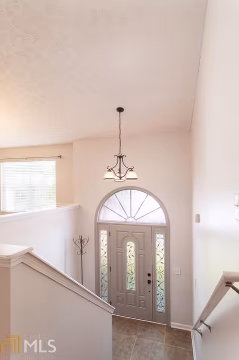 View down into an entryway with a decorative front door and arched transom, hanging light fixture, stair railing, and tiled floor.