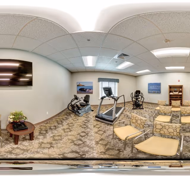 A small senior fitness room with a treadmill and exercise bikes, seating chairs, a wall-mounted TV, and framed artwork.