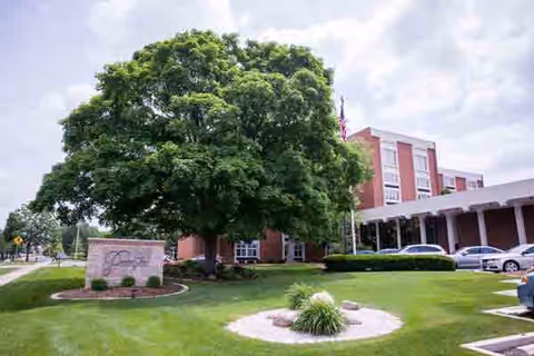 Exterior view of Proctor Place Senior Living building with a large tree and manicured lawn.