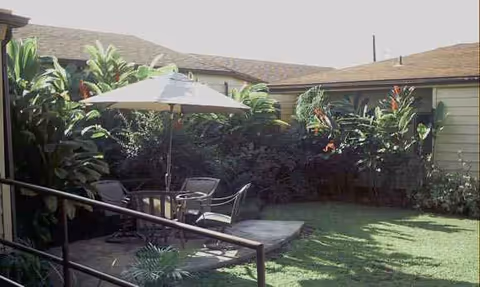 Outdoor patio with umbrella, chairs, and lush tropical plants in a fenced backyard.