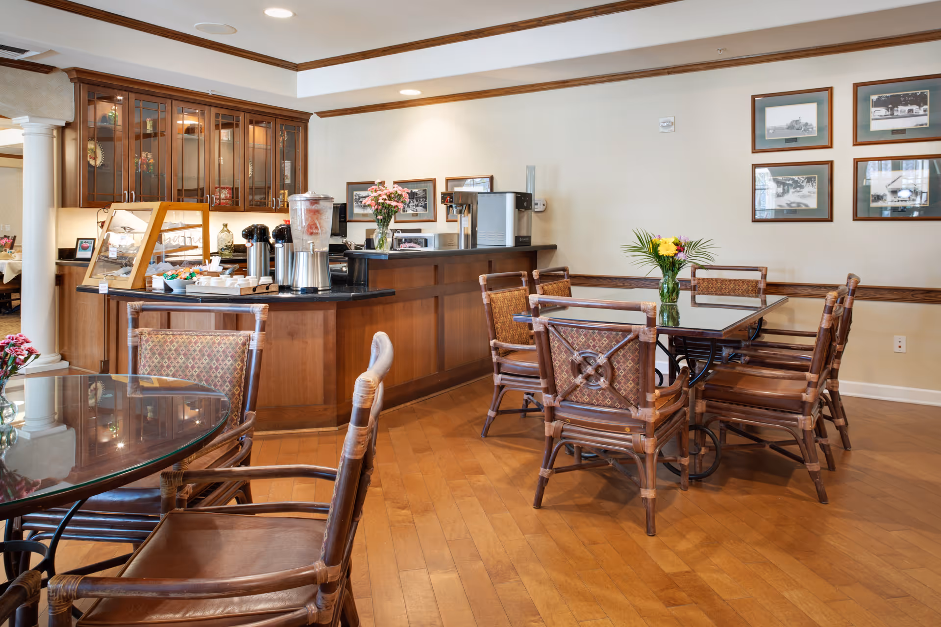 Bright dining area with wooden tables and chairs and a service counter with coffee dispensers and flowers.