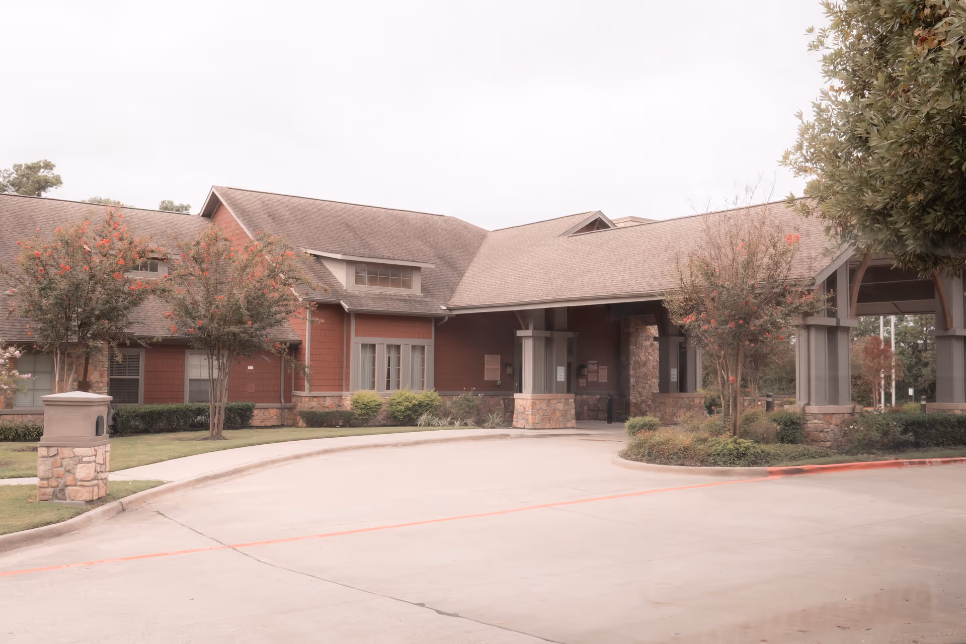 Exterior view of The Broadmoor At Creekside Park building with a covered entrance, stone and wood siding, surrounded by trees and landscaping.