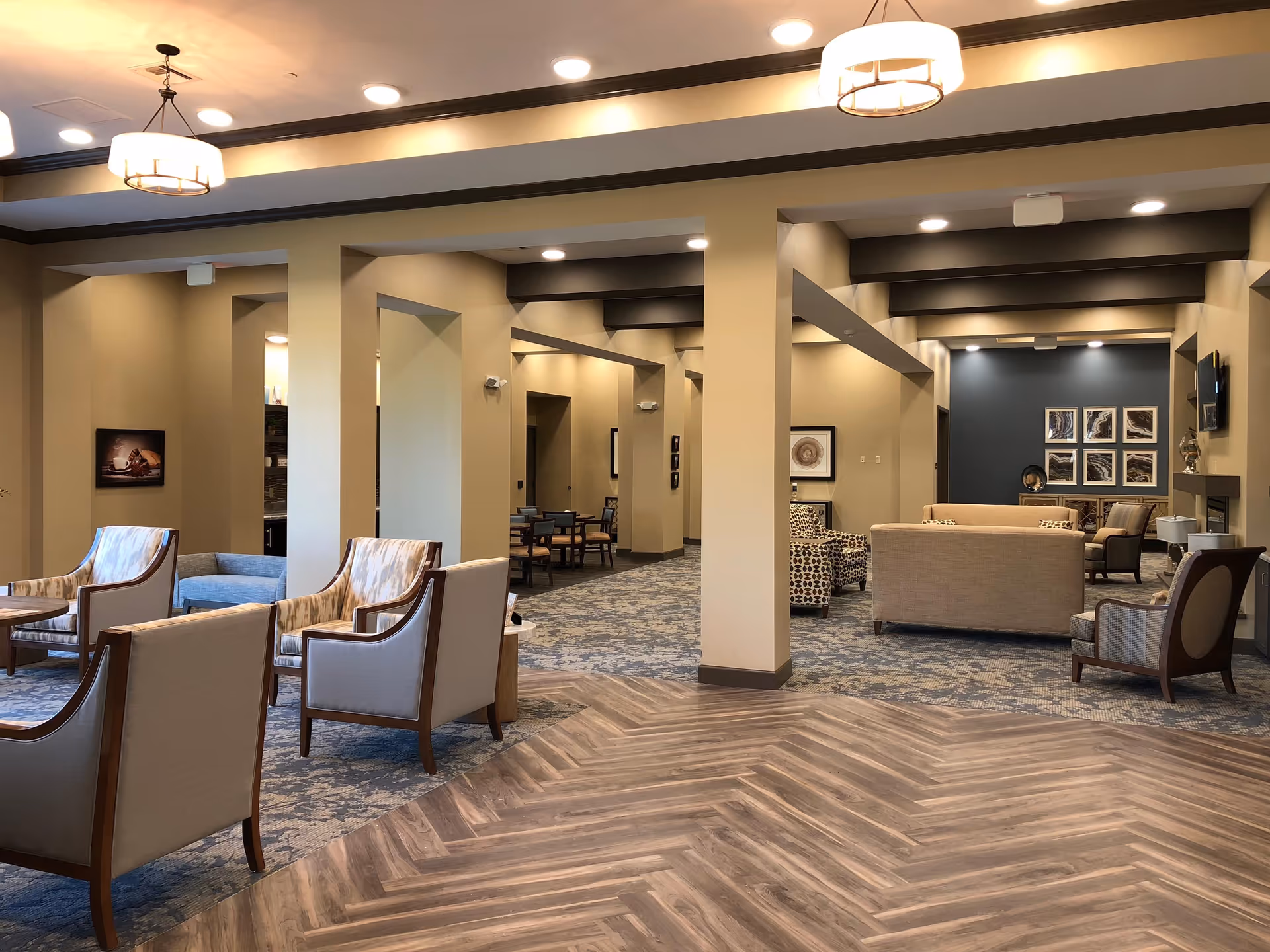 Spacious furnished common lounge area with multiple seating arrangements, tables, and warm overhead lighting.