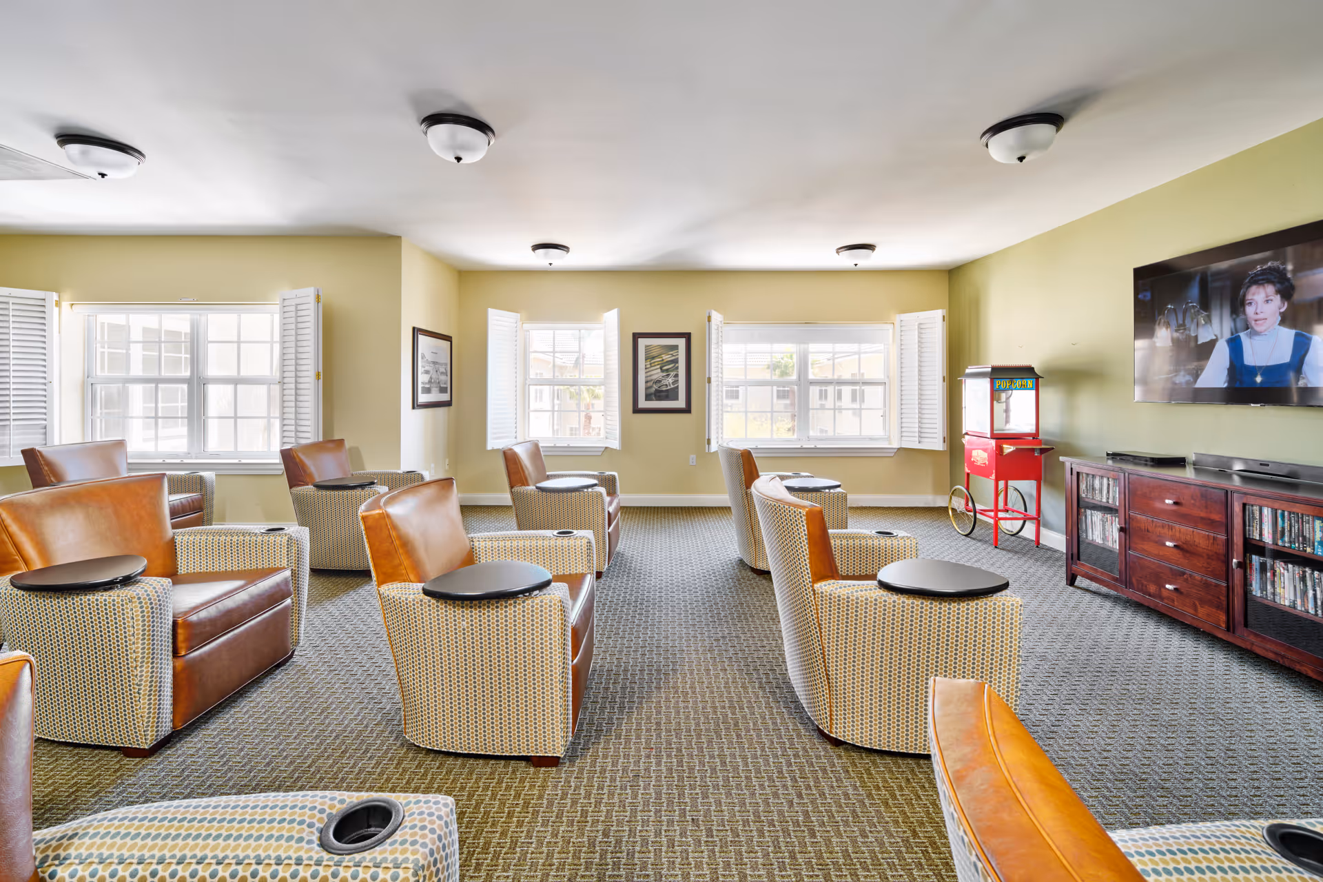 Bright common lounge with leather and patterned armchairs arranged facing a wall-mounted TV and a popcorn machine.