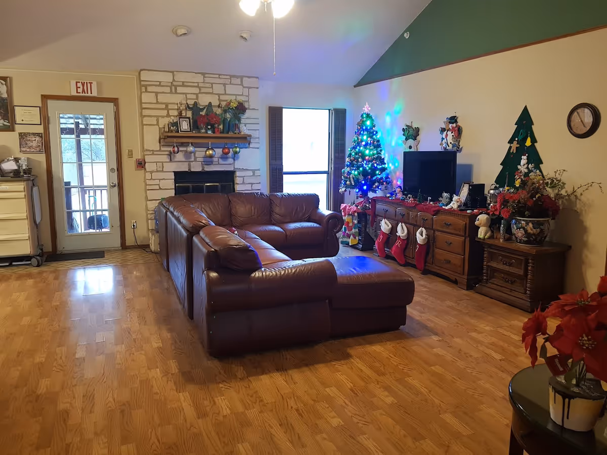 Cozy living room with a brown leather sectional, stone fireplace, TV stand and a decorated Christmas tree.