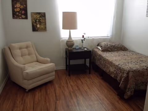 A small bedroom in a senior living facility with a bed, chair, and lamp.