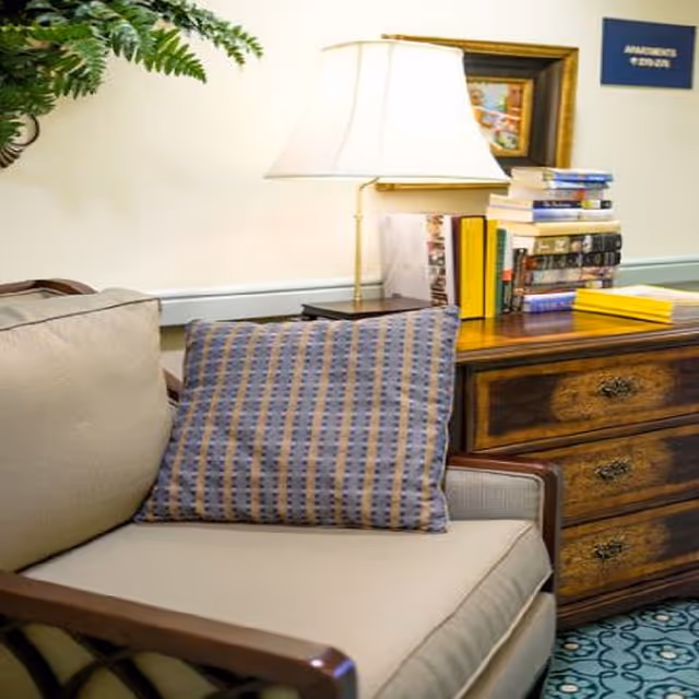 Upholstered armchair with a striped throw pillow beside a wooden side table topped with a lamp and stacked books.