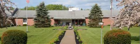 Brick senior living facility facade with a central walkway and trimmed lawn.