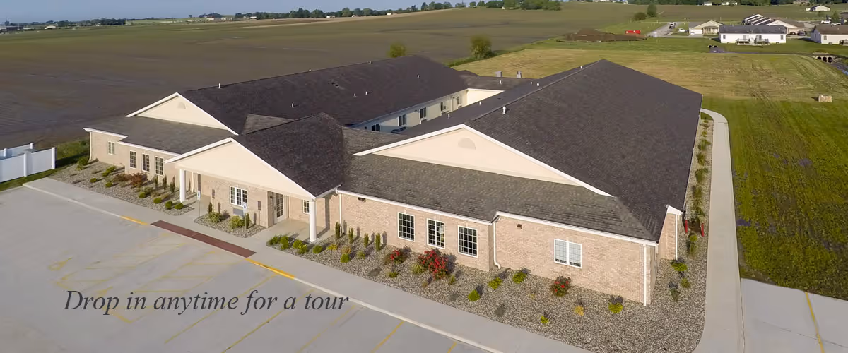 Aerial view of a single-story brick memory care building with a parking lot and surrounding open fields.