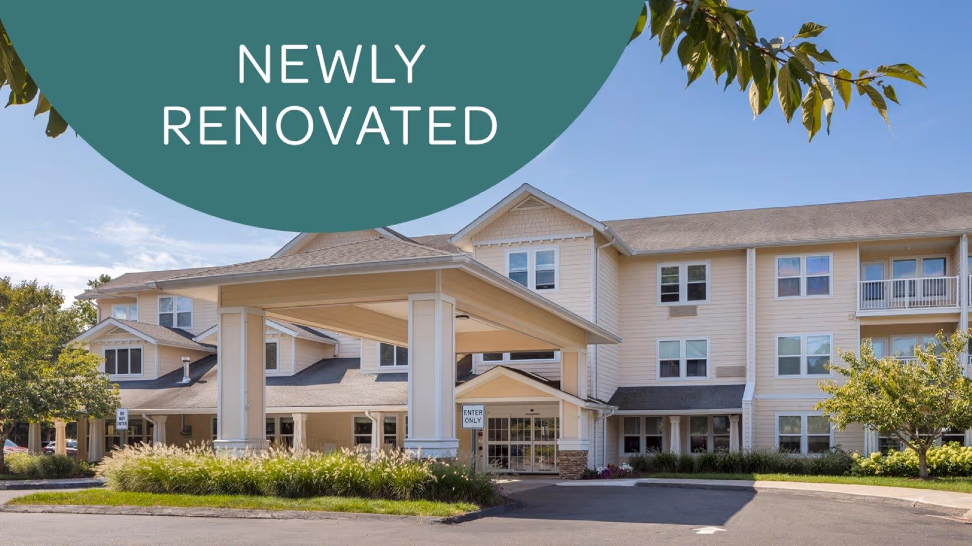 Front exterior of a newly renovated three-story senior living building with a covered porte-cochere entrance and surrounding landscaping.