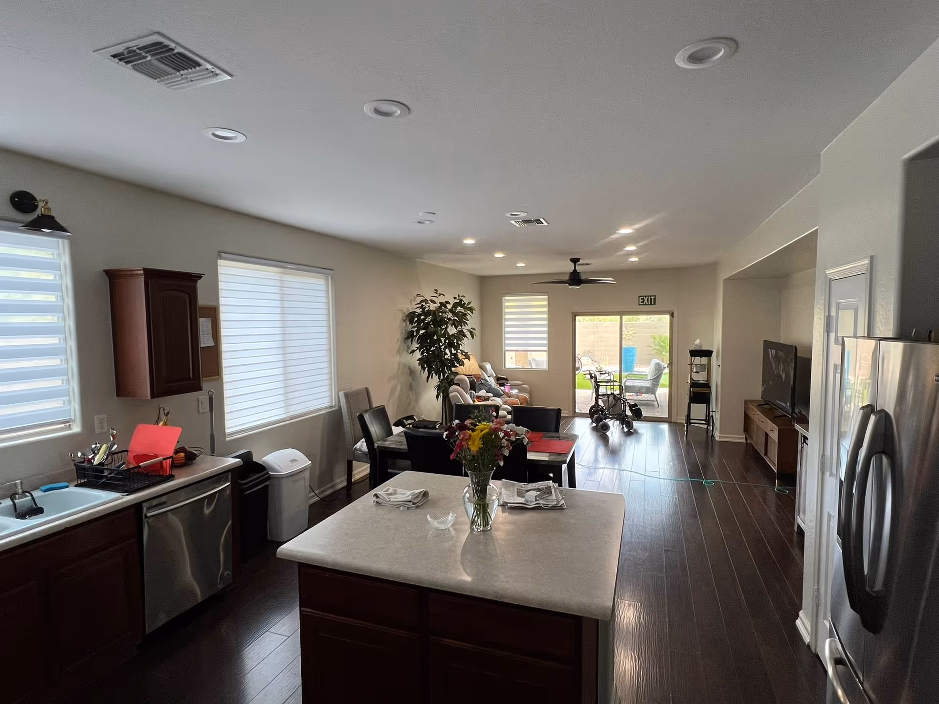 Open-plan interior showing a kitchen island in the foreground and a living area with seating and a walker near sliding doors.