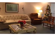 A cozy living room with sofa, chairs, coffee table, and a Christmas tree.