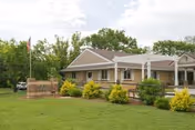 Front exterior view of Arvada Care and Rehabilitation Center with landscaped entrance and flag.