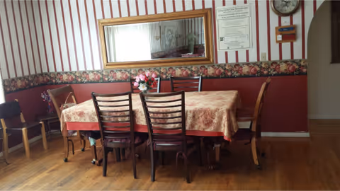 A dining room with a table, chairs, floral wallpaper, and a mirror.