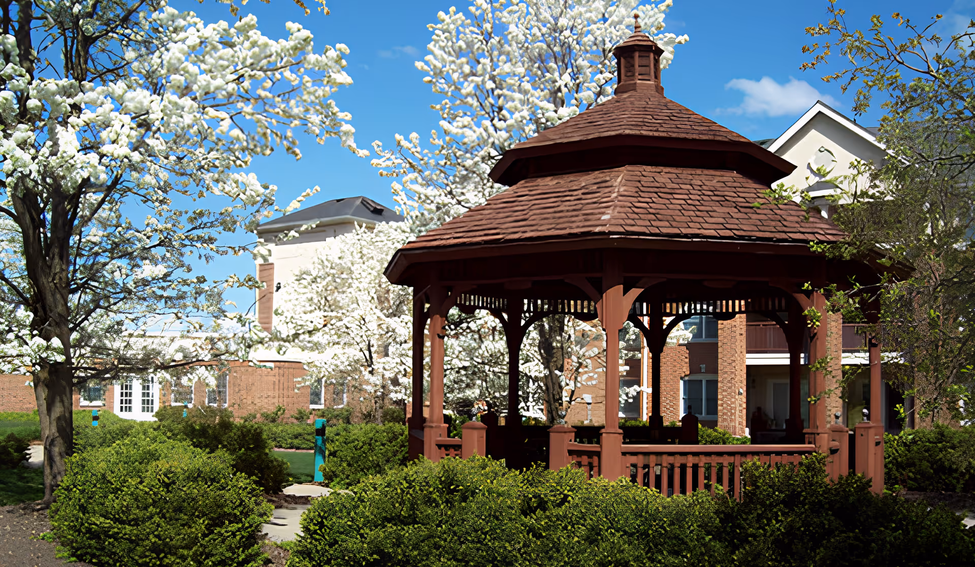 Wooden gazebo in a landscaped courtyard with blooming trees and the Hartsfield Village building in the background.