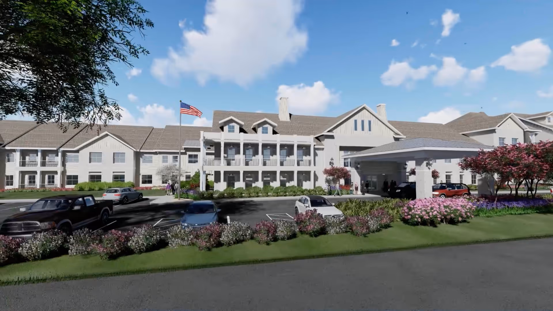 Front exterior view of The Claiborne at Brickyard Crossing senior living facility with a large building featuring multiple windows, a covered entrance, an American flag on a flagpole, several parked cars, landscaped bushes, and flowering plants under a partly cloudy blue sky.