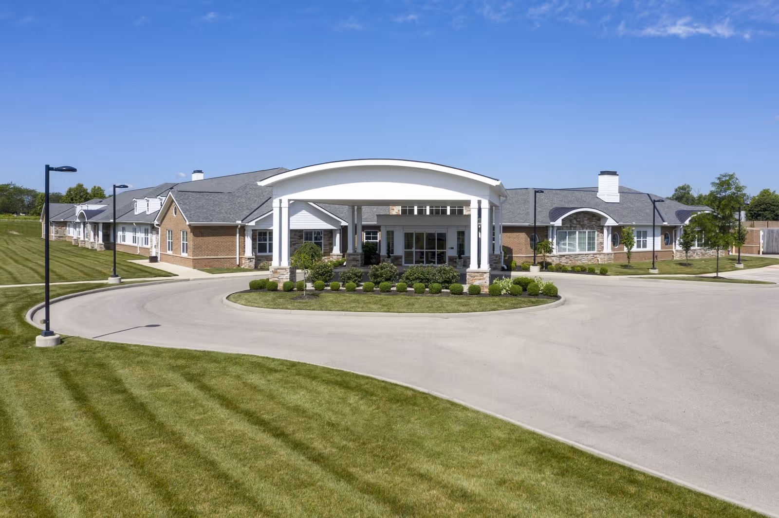 Front exterior view of a single-story senior living facility building with a covered entrance, well-maintained lawn, and clear blue sky.