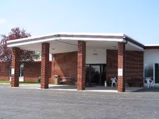 Brick-faced building entrance with a covered drop-off area and outdoor seating.
