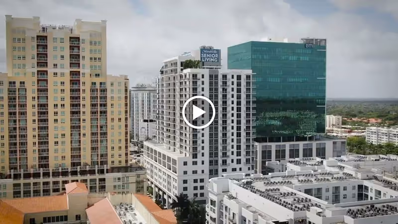 Aerial view of the Mirabelle Senior Living high-rise and surrounding downtown buildings.