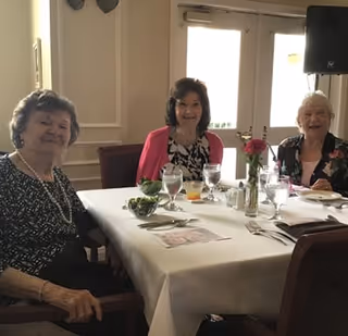 Three women seated at a dining table in a bright dining room, smiling at the camera.