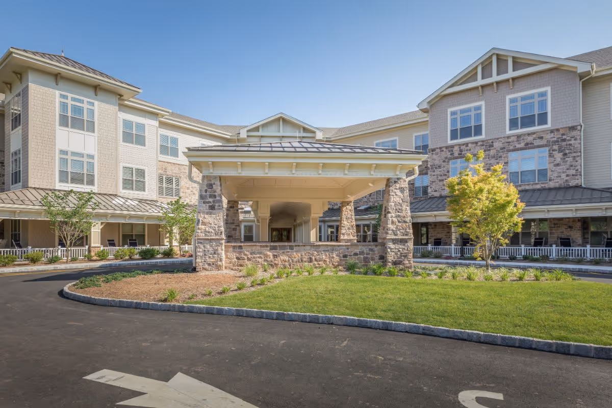 Front entrance of a multi-story senior living facility with a covered porte-cochère and landscaped circular driveway.