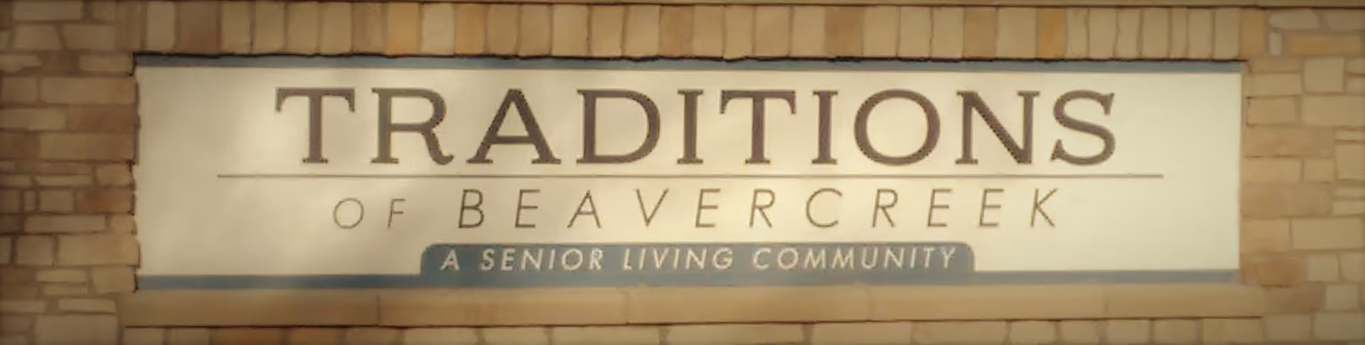 Sign on a brick wall that reads 'TRADITIONS OF BEAVERCREEK A SENIOR LIVING COMMUNITY'.