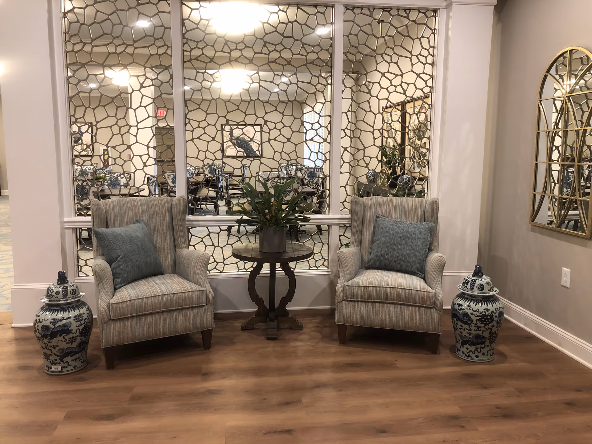 Two striped armchairs flank a small table with a potted plant, separated by decorative screen.