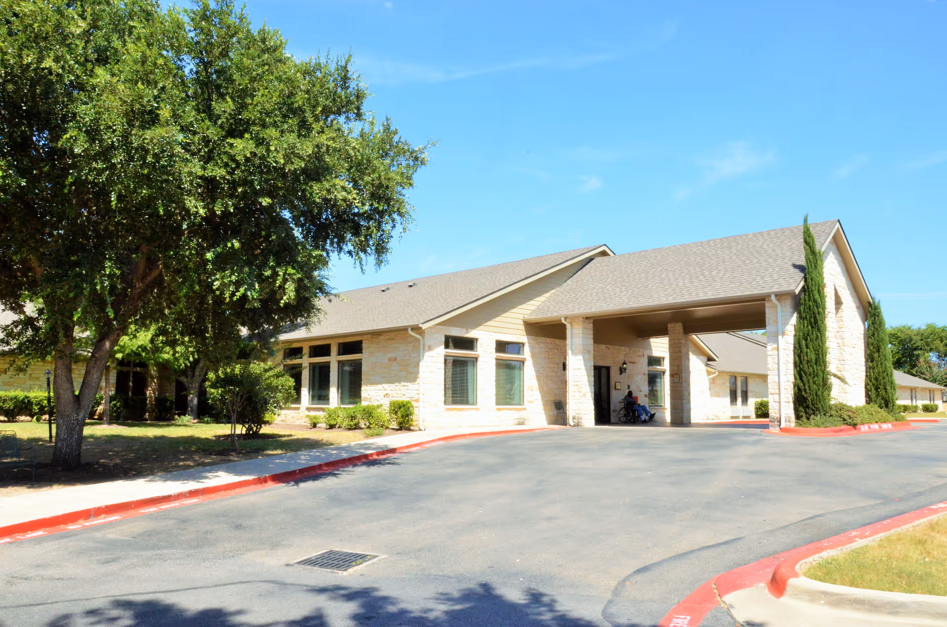 Exterior view of Harker Heights Nursing & Rehabilitation facility showing a single-story building with a covered entrance, surrounded by trees and landscaping under a clear blue sky.