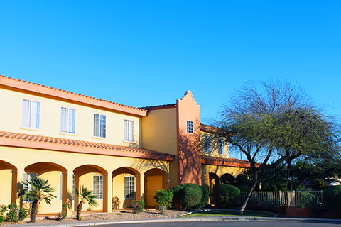 Exterior view of a yellow stucco building with arches and palm trees.