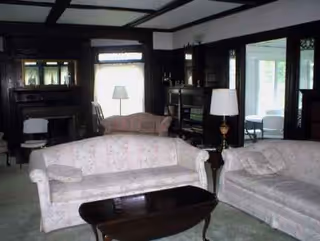 Dim living room with light floral sofas, coffee table, fireplace, and lamps.
