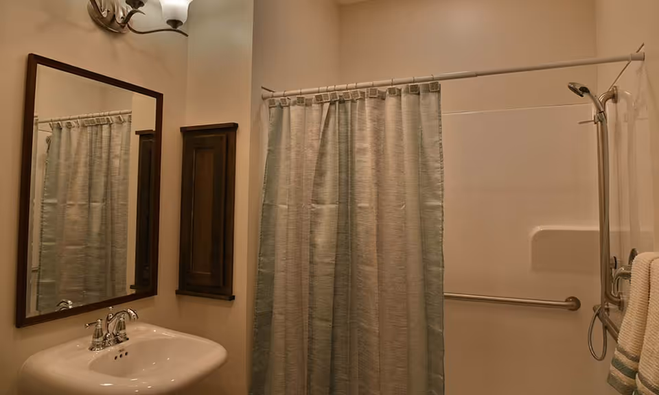 Bathroom with a sink and mirror on the left and a shower with a curtain and grab bar on the right.