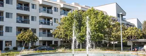 Exterior view of Regents Point facility with a fountain, trees, and parked cars.