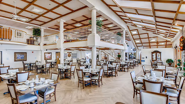 Spacious dining room with multiple set tables, a high coffered ceiling, and an open mezzanine level.