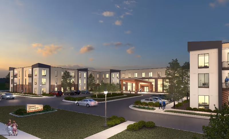 Modern senior living facility exterior at dusk with entrance and parked cars