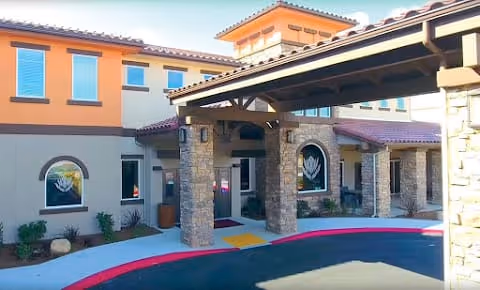 Exterior view of HarborChase of Palm Coast building entrance with stone pillars, covered driveway, and windows with decorative artwork.
