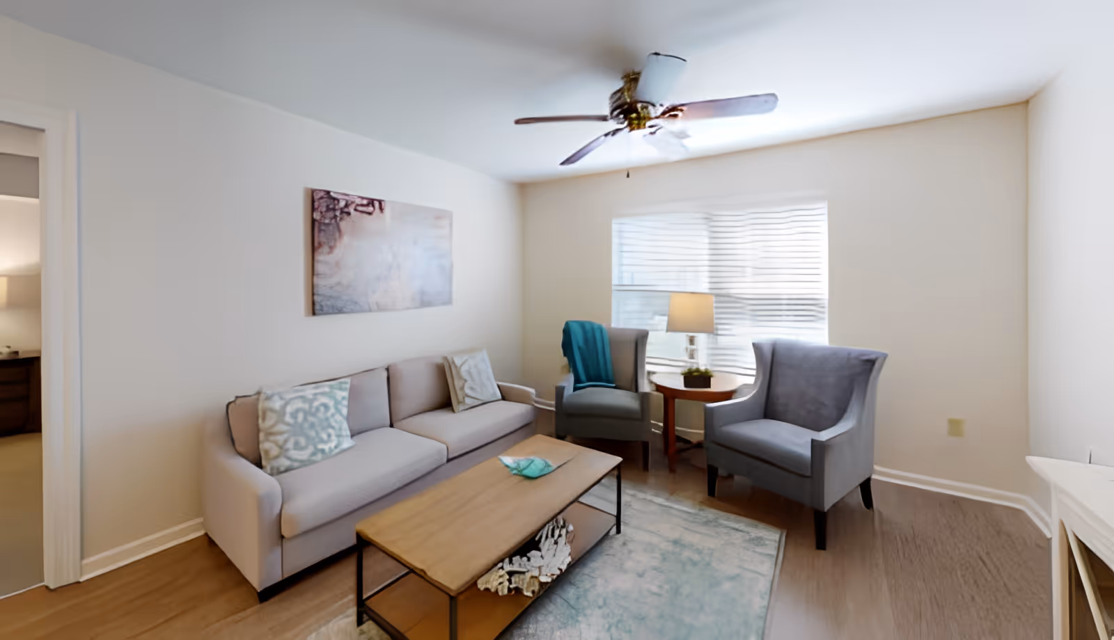 Bright living room with a sofa, two armchairs, a coffee table, side table with a lamp, and a ceiling fan.