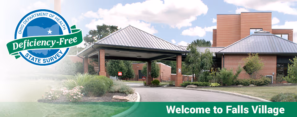 Exterior view of Falls Village Skilled Nursing & Rehabilitation showing a brick building with a covered entrance driveway, surrounded by greenery and a partly cloudy sky. A badge on the left side indicates a Deficiency-Free State Survey by the Ohio Department of Health. The bottom green banner reads 'Welcome to Falls Village.'