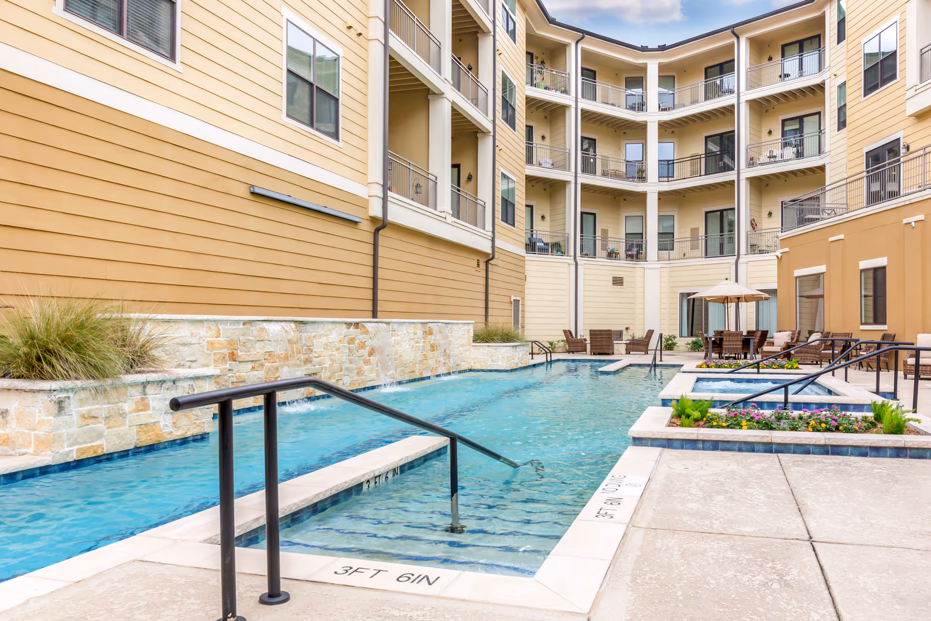Outdoor courtyard with a rectangular swimming pool, lounge chairs, planters and balconies of a multi-story senior living building.