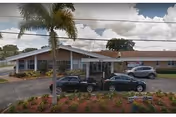 Single-story senior living facility building with a covered entrance, palm tree in front, and cars parked along the driveway.