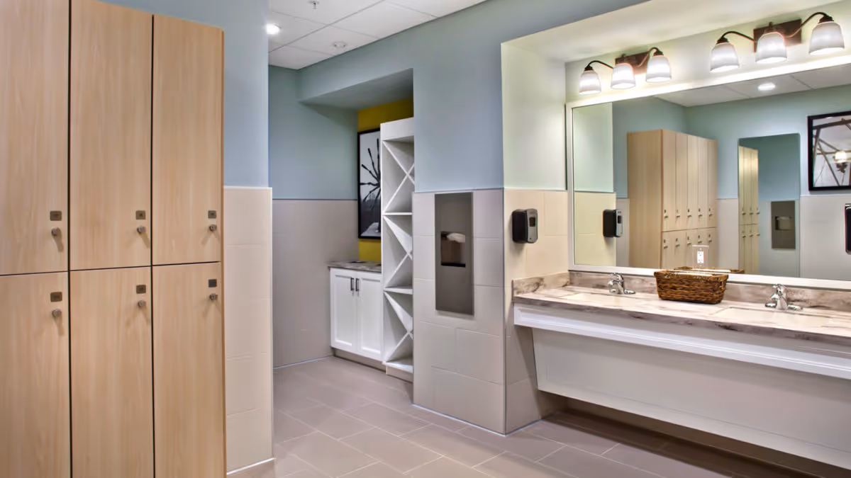 Locker-room style bathroom with wooden lockers, a double-sink vanity beneath a large mirror, and open shelving cubbies.