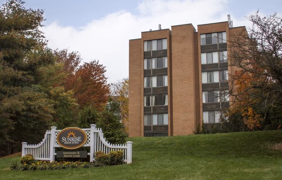 Multi-story brick senior living building with a lawn and a 'Sunrise Senior Living' sign in front.