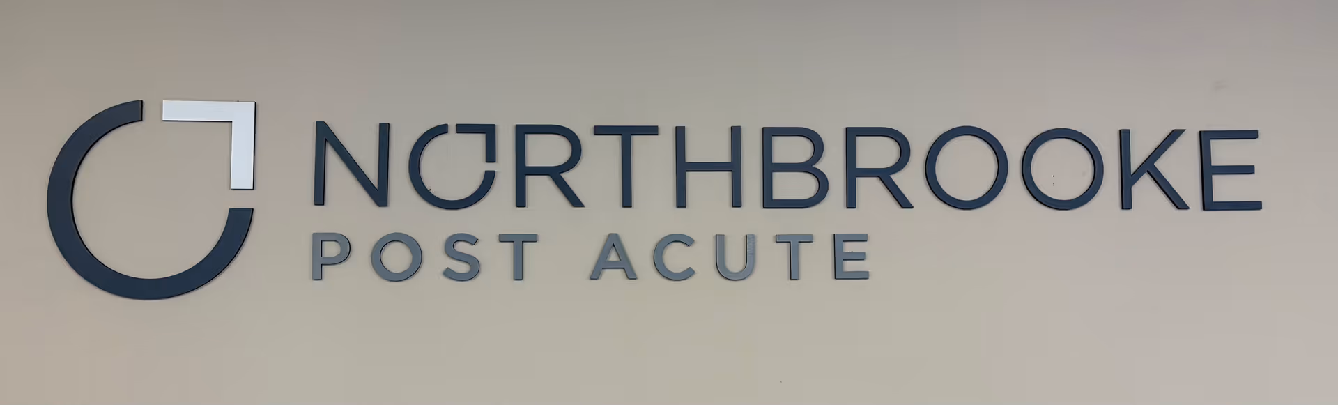 Wall sign reading "NORTHBROOKE POST ACUTE" with a circular logo mounted on a light-colored wall.
