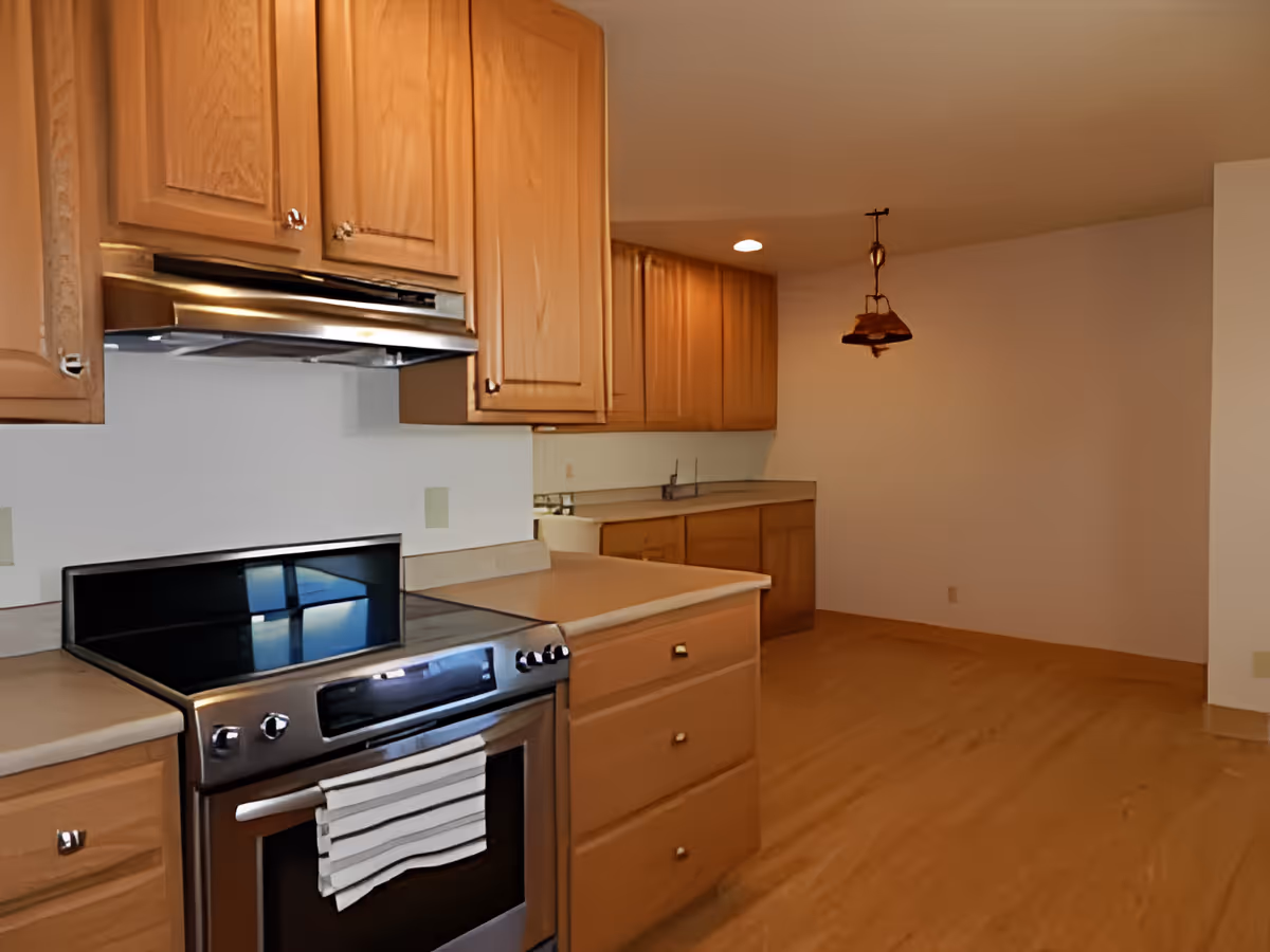 Spacious kitchen with wooden cabinets, a stainless steel stove, countertop island, and an open dining area with a hanging light fixture.