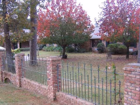 Brick fence lines a grassy yard with autumn trees and a building in the background.