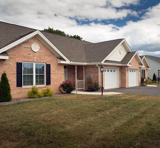 Brick senior living residence with attached garages, manicured lawn, and a clear front entrance.