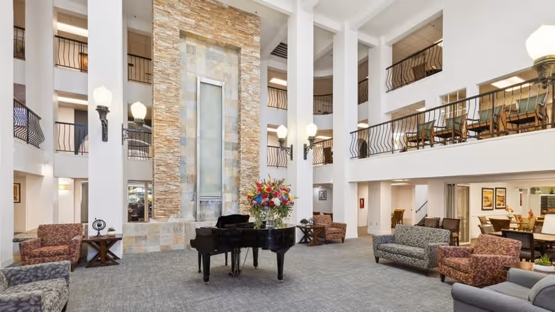 Spacious multi-story lobby/atrium with a grand piano, seating areas, balconies, and a tall stone water feature.