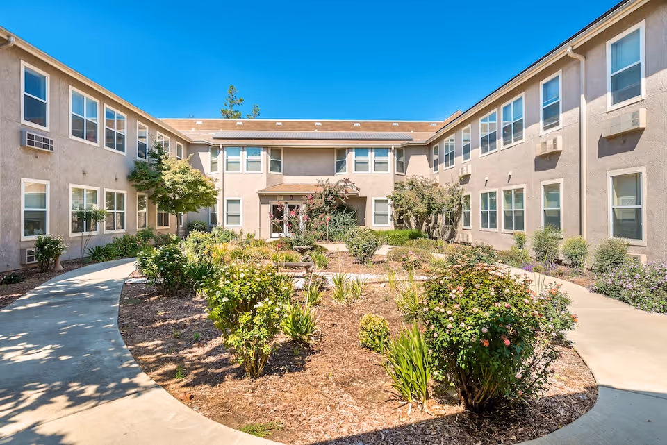 Sunlit landscaped courtyard with walkways surrounded by a two-story senior living building.