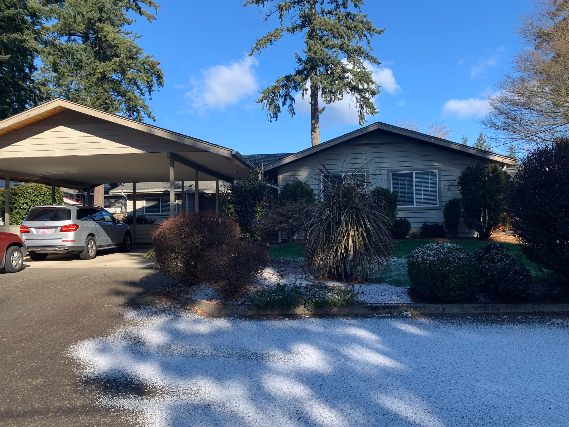 Single-story house with a covered carport, parked cars, and a light dusting of snow on the driveway and front landscaping.