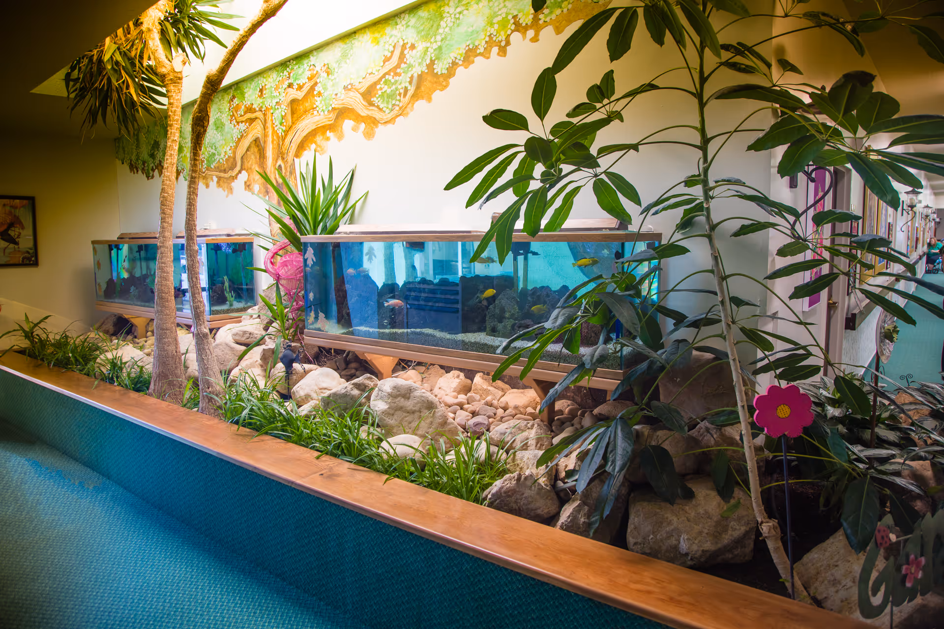 A decorated interior corridor featuring built-in aquariums surrounded by rocks, plants, and a painted tree mural.
